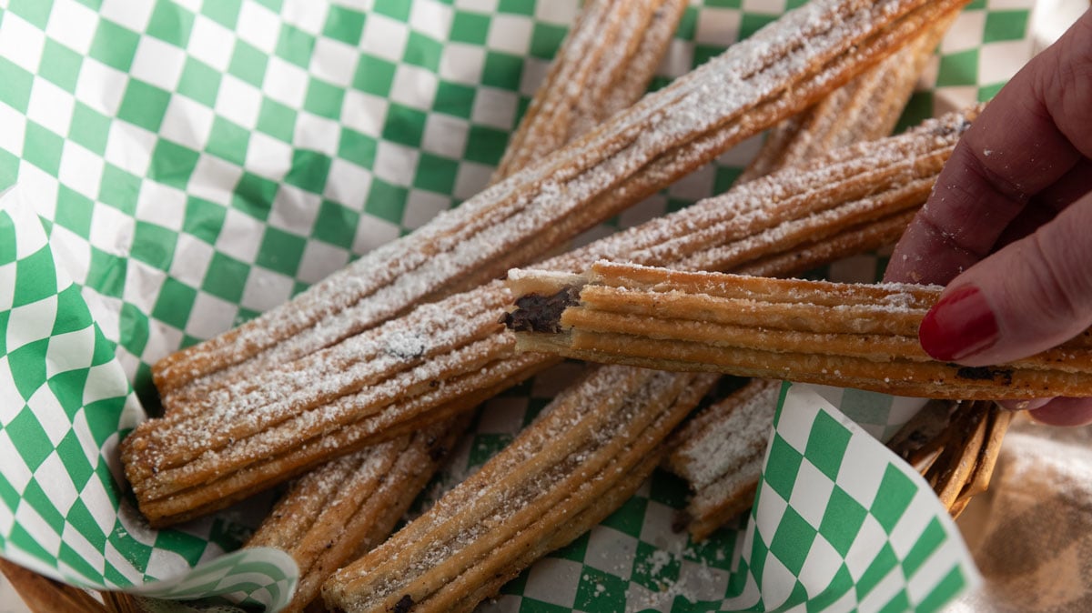 Woman's hand holding an air fried churro with a bite out of it.
