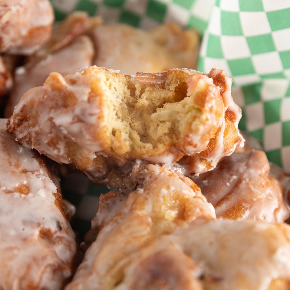 Golden apple fritters stacked with one with a bite taken out.