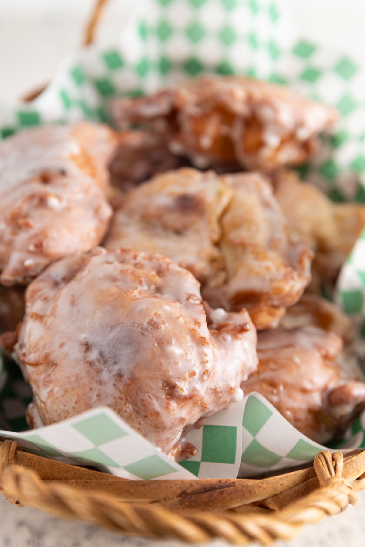 Apple fritters stacked in a basket with green and white checked paper.