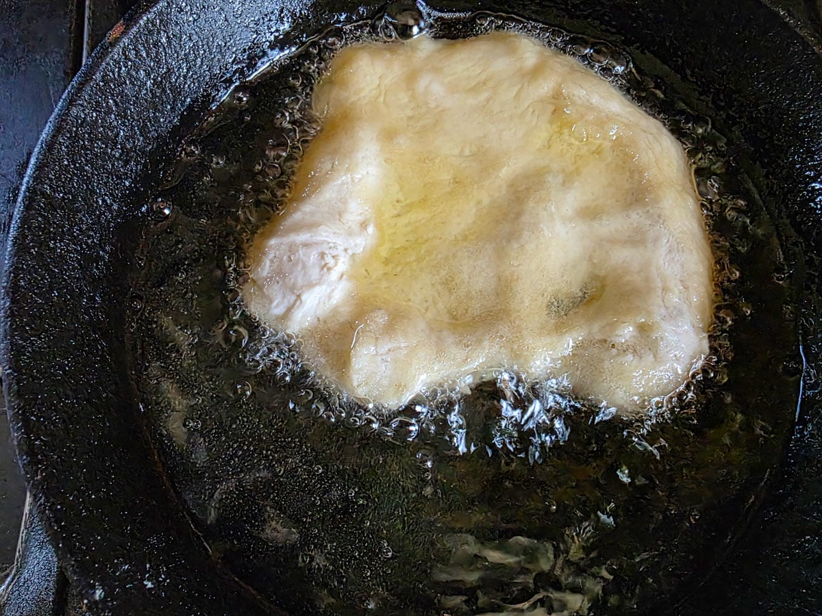 Flattened dough disk frying in hot oil.