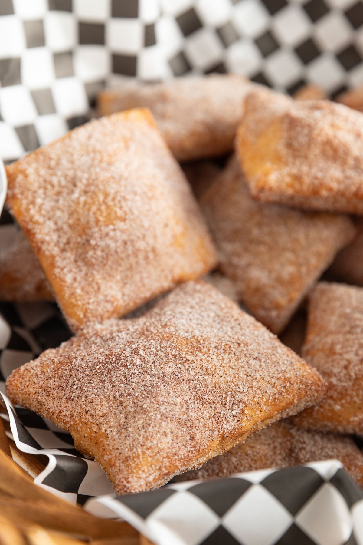 Cinnamon sugar dipped sopaillas in a basket with black and white checked paper.