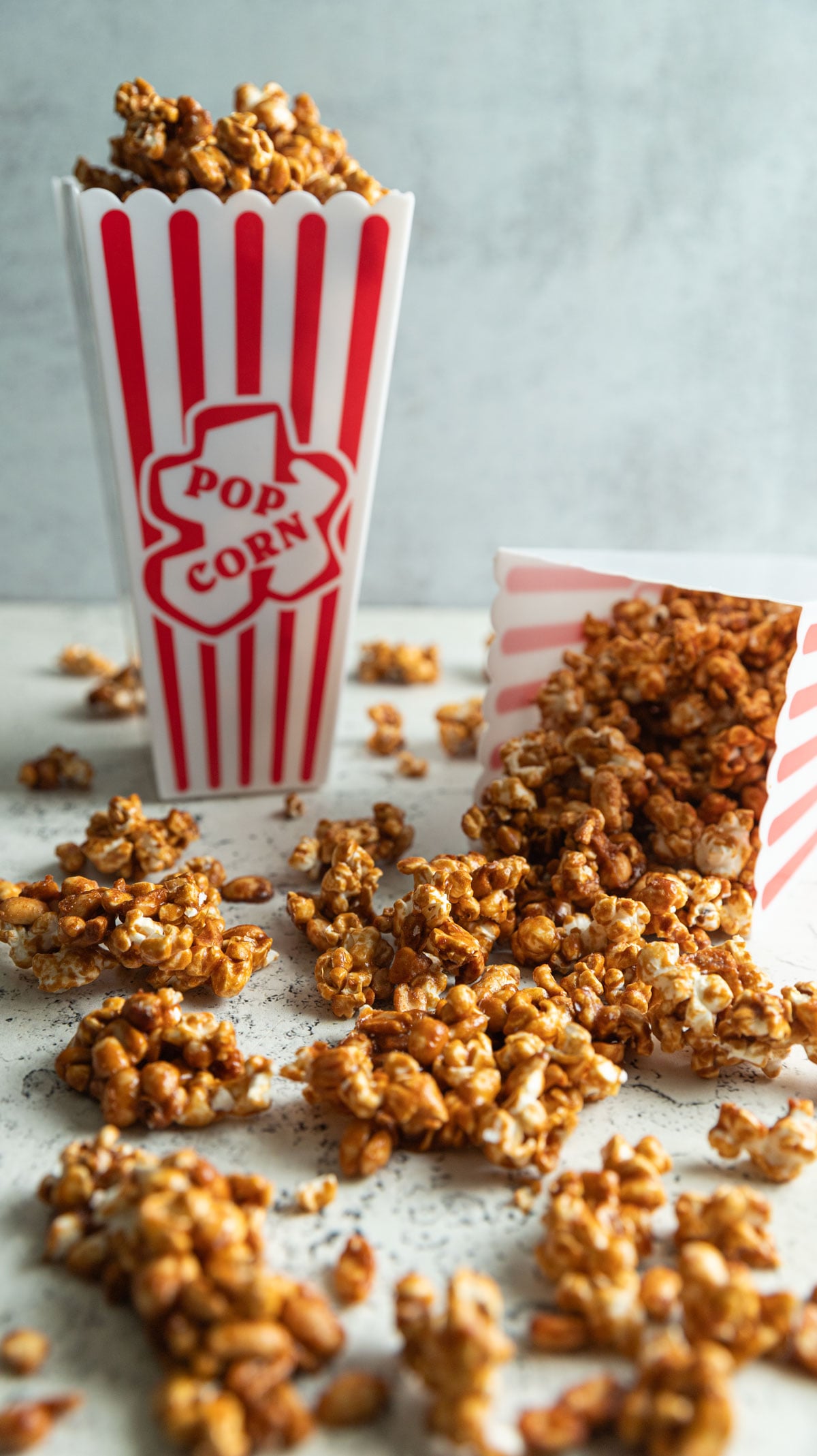 Caramel corn spilling out of a popcorn box onto white board.