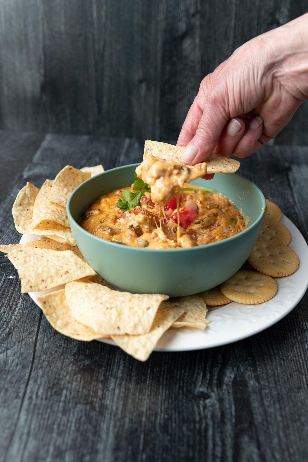 Woman's hand dipping a tortilla chip into queso dip.