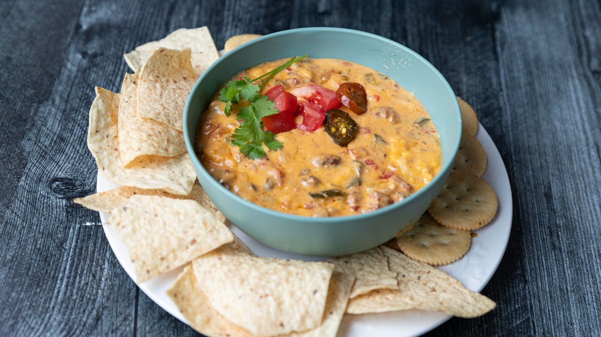 Green bowl filled with queso dip garnished with tomatoes, peppers and cilantro.