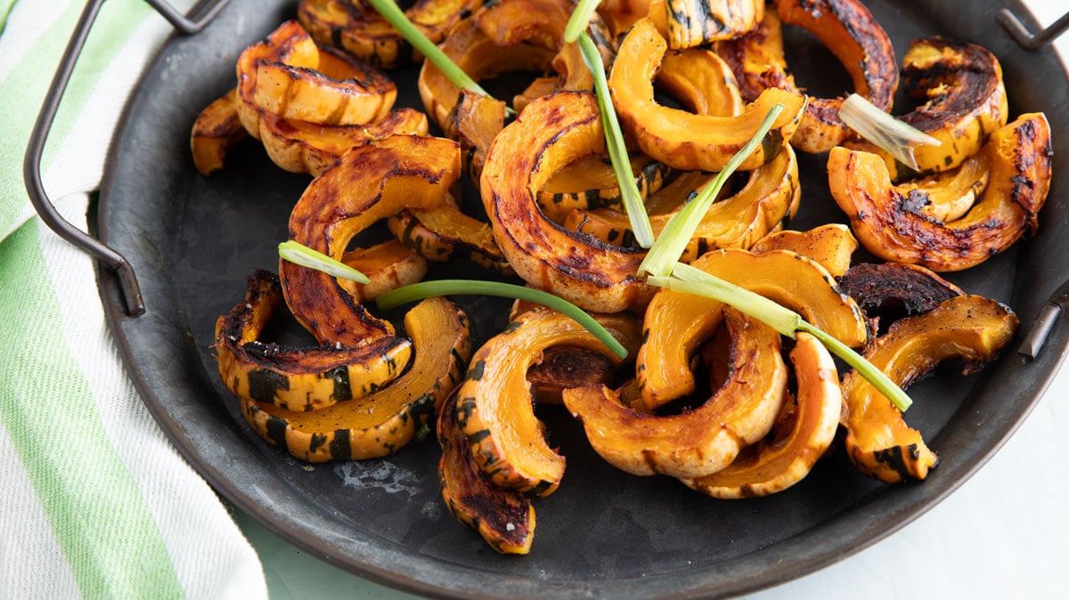 Delicata squash on a pewter tray with greens for garnish.
