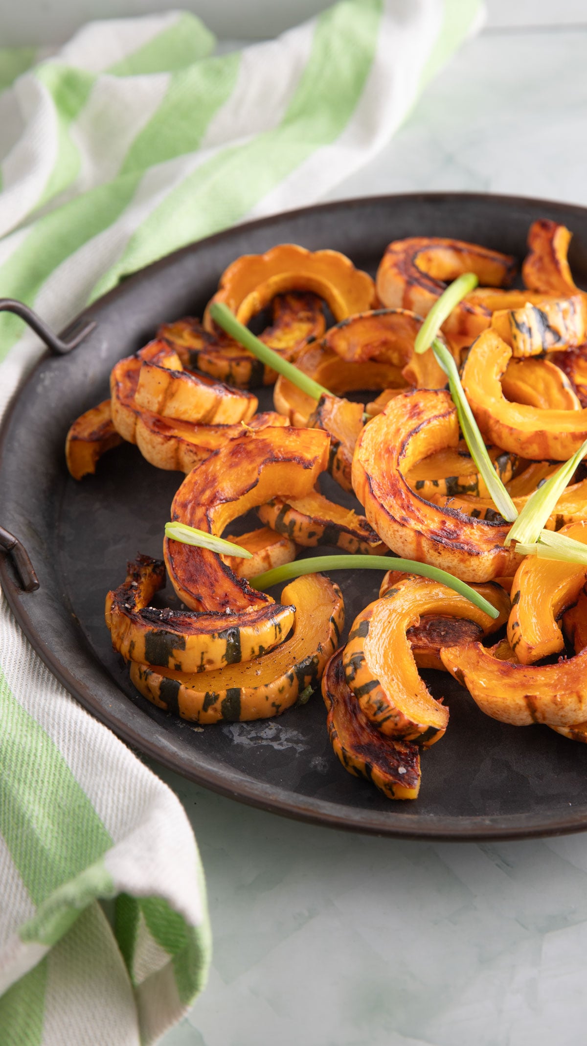 Roasted delicata squash with caramelized edges sliced on a pewter tray.