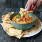 Woman's hand dipping a tortilla chip into a bowl of queso dip.