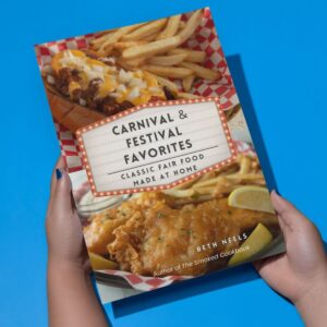 Woman holding a paperback version of Carnival & Festival Favorites with a blue background.