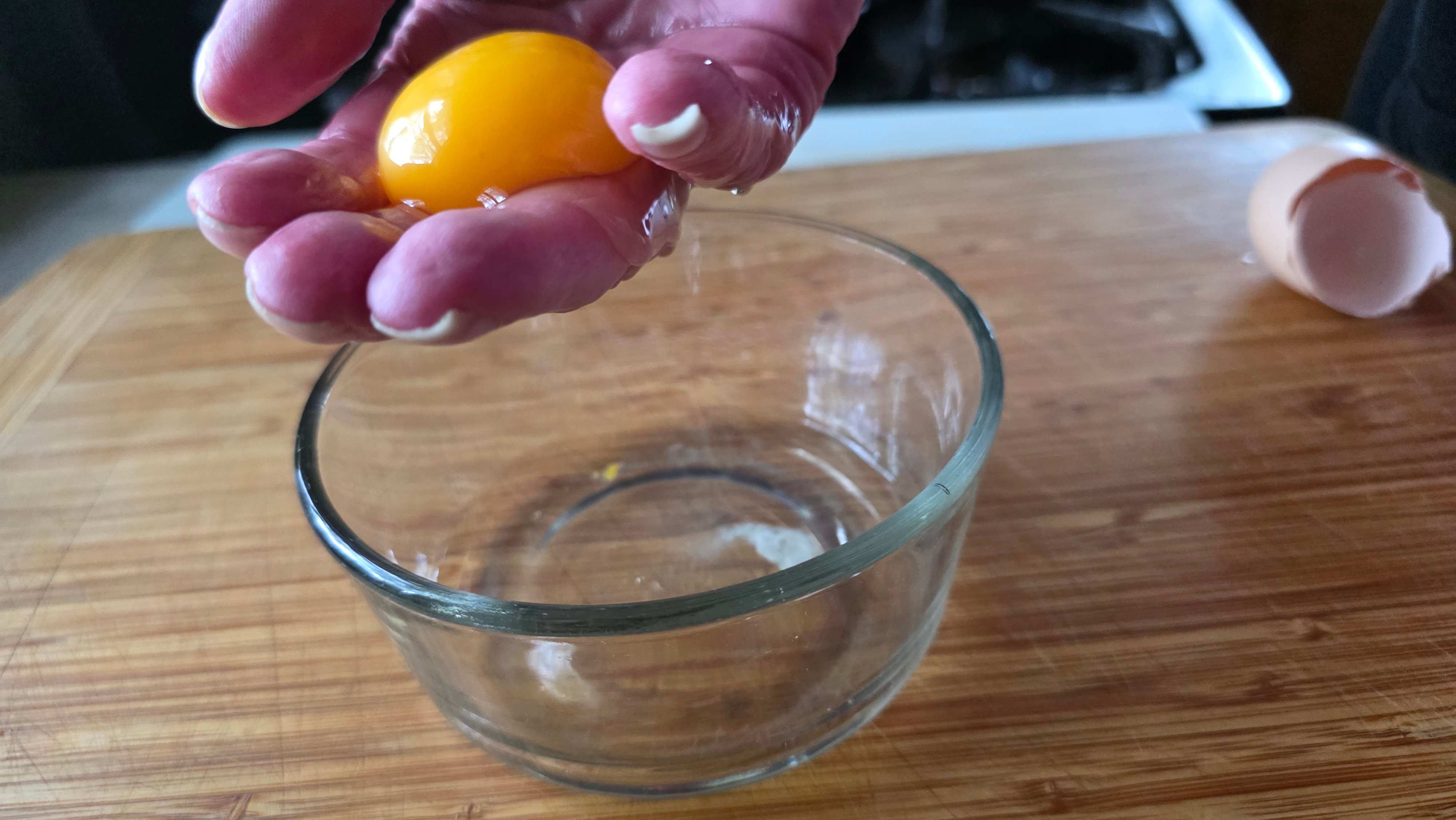 Woman's hand with an egg yolk on her fingers and the egg white draining into a bowl.