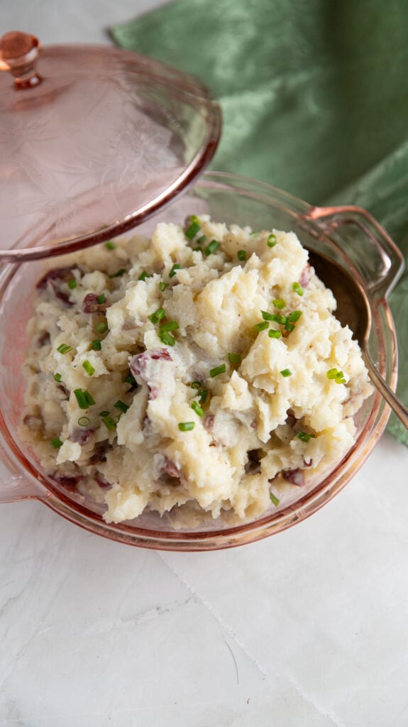 Pink covered bowl with red mashed potatoes garnished with chives.
