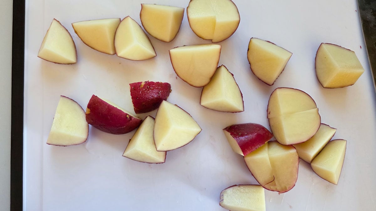 Quartered potatoes on a white cutting board.