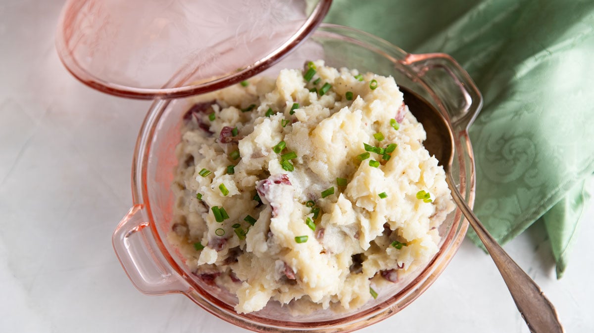 Pink depression glass covered serving dish with mashed potatoes.